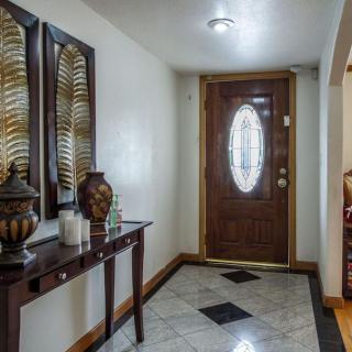 A welcoming entryway with a wooden front door, decorative wall art, and a table adorned with vases.