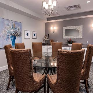 A well-decorated dining room with a glass table, brown chairs, a chandelier, and wall decor.