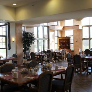 A spacious dining area with several tables and chairs, elegantly decorated and well-lit by large windows.