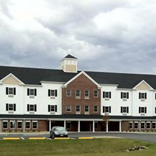 A multi-story building with a symmetrical design, likely a hotel, stands under an overcast sky with a car parked in front.