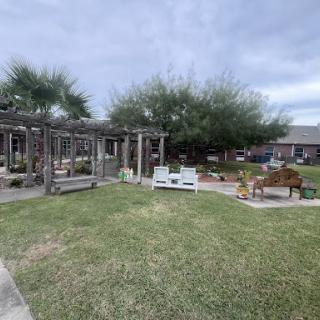 A serene backyard setup featuring a pergola, outdoor seating, and lush greenery.