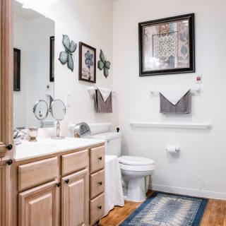A well-decorated bathroom featuring a sink, toilet, mirror, wall art, and neatly arranged towels.