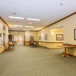A spacious hallway with carpeted flooring, adorned with artwork and furnished with tables and chairs.