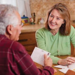 A woman and an elderly person having a conversation at a kitchen table, exchanging letters.