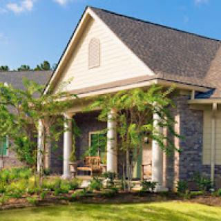 A beautifully designed modern house showcasing a blend of stone and siding with lush landscaping.