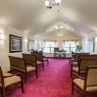 A well-lit room with rows of chairs arranged on a vibrant red carpet, featuring large windows and decorative elements.