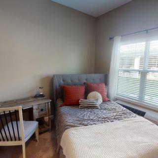Cozy bedroom with a neatly made bed, a small desk and chair by the window.
