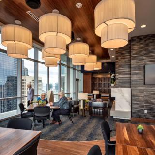A modern restaurant interior with large windows offering a city view, featuring stylish hanging lights and wood accents.