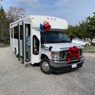 A white shuttle bus adorned with balloons and a large red ribbon parked outdoors.