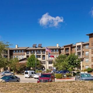 A multi-story building with a parking lot and cars in front, under a clear blue sky with a few clouds.
