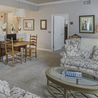 A cozy living and dining area with floral patterned sofas, a wooden dining table, and framed artwork on the walls.