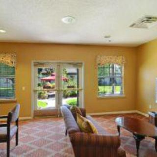 A cozy living room with a sofa, chairs, and coffee table, featuring large windows and a glass door opening to a garden.