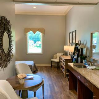 A cozy and stylish interior room with wooden flooring, featuring elegant furniture, a decorative mirror, and a view through the window.