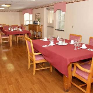 A dining area with several tables set for a meal, featuring red tablecloths and wooden chairs.