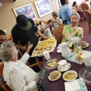 Seniors enjoying a meal together with a selection of pastries being served.
