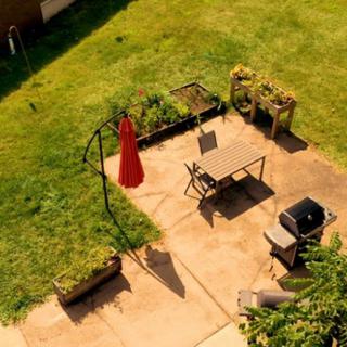 Aerial view of a patio with a table, chairs, a red umbrella, grill, and planters in a backyard setting.
