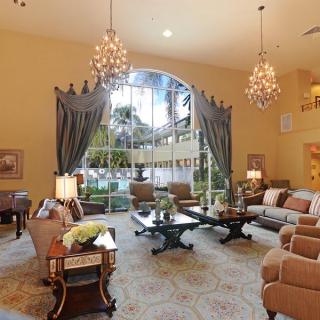 A luxurious living room with elegant chandeliers, plush furniture, and a large window with draped curtains.