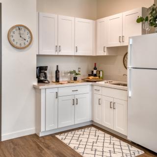A modern kitchen with white cabinetry and appliances, featuring a coffee maker, wall clock, and decorative elements on the countertop.