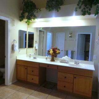 A well-lit bathroom with a large mirror, wooden vanity, and decorative flowers.