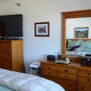 A cozy bedroom featuring a dresser with a mirror, a TV, and neatly made bed.