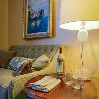 A cozy living room setup featuring a sofa, table with a bottle and glasses, and a warm lamp.