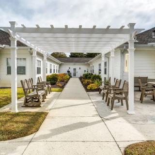 A walkway with a pergola, surrounded by outdoor seating and landscaped gardens.