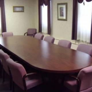 A conference room with a large wooden table surrounded by cushioned chairs.