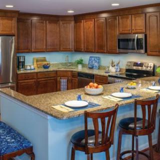A modern kitchen featuring wooden cabinetry, granite countertops, and a cozy dining area with bar stools.