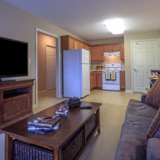 A cozy living room with a view into the kitchen area, featuring a sofa, coffee table, and television.