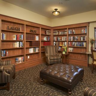 A cozy library room featuring wooden bookshelves filled with books, leather armchairs, and a large ottoman.