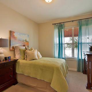 A cozy bedroom with a green bedspread, wooden furniture, and sheer blue curtains.