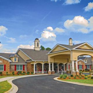 A picturesque residential building with a circular driveway under a bright, partly cloudy sky.