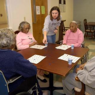A volunteer assists elderly individuals playing bingo at a nursing home.