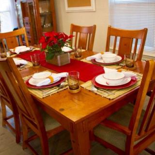 A warmly set dining table with a red runner and floral centerpiece, ready for a meal.