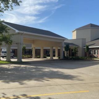 A commercial building with a covered driveway and parking area on a sunny day.
