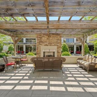 A cozy outdoor patio with a pergola and a central fireplace surrounded by comfortable seating.