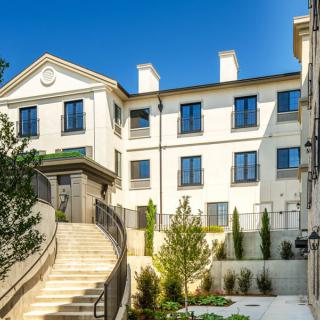 A modern residential building with white walls and large windows, featuring a staircase and landscaped greenery.