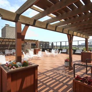 A spacious city rooftop terrace with a pergola and outdoor seating on a sunny day.