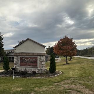 A welcoming sign alongside a quiet road, with a backdrop of cloudy skies and an autumn-colored tree.