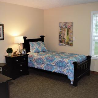 A cozy bedroom featuring a single bed with patterned bedding, a nightstand with a lamp, and decorative artwork on the wall.