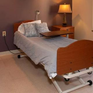 A hospital-style bed with a tray table in a warmly lit room.