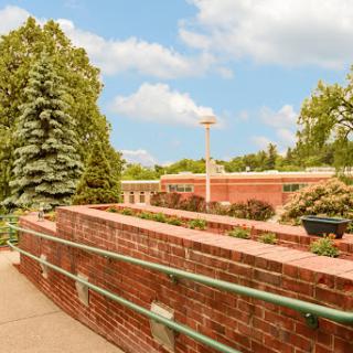 A scenic view of a landscaped area featuring brick structures and lush greenery under a blue sky.