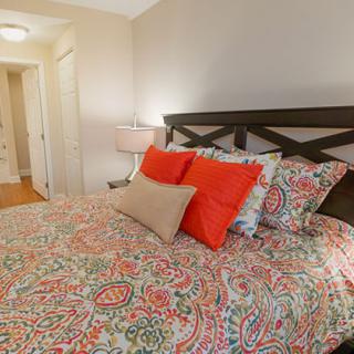 A cozy bedroom featuring a bed with colorful bedding and accent pillows, complemented by a bedside lamp.