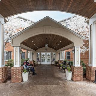 A covered entrance walkway with benches and potted plants leading to a building.