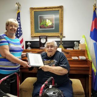 A woman presents a certificate to an elderly man in a warm indoor setting.