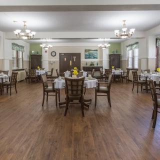 An empty dining room with neatly arranged tables and chairs, featuring a wooden floor and elegant chandeliers.