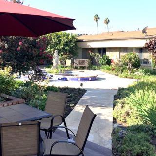A tranquil garden patio with outdoor furniture and a red umbrella on a sunny day.