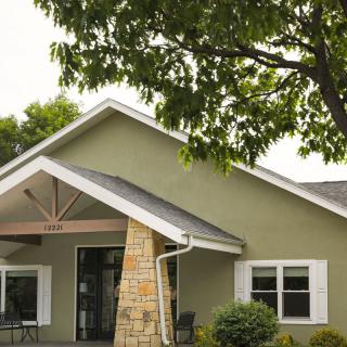 A quaint green house with a sloped roof and stone pillar under a tree.