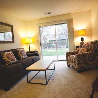A cozy living room with a sofa, armchair, and sliding door leading to the backyard.