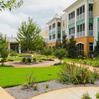 A modern building surrounded by a well-maintained garden with lush greenery and paved pathways under a cloudy sky.